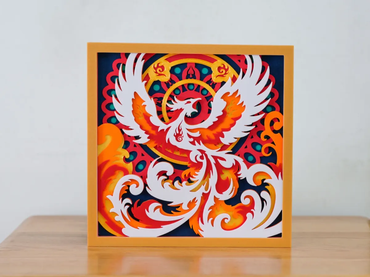 Tableau en couches Phénix de feu : un phénix blanc aux ailes déployées et aux flammes orange devant un mandala rouge et bleu marine, dans un cadre doré